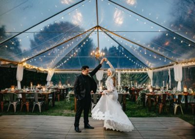 a bride and groom dancing under a clear top wedding tent